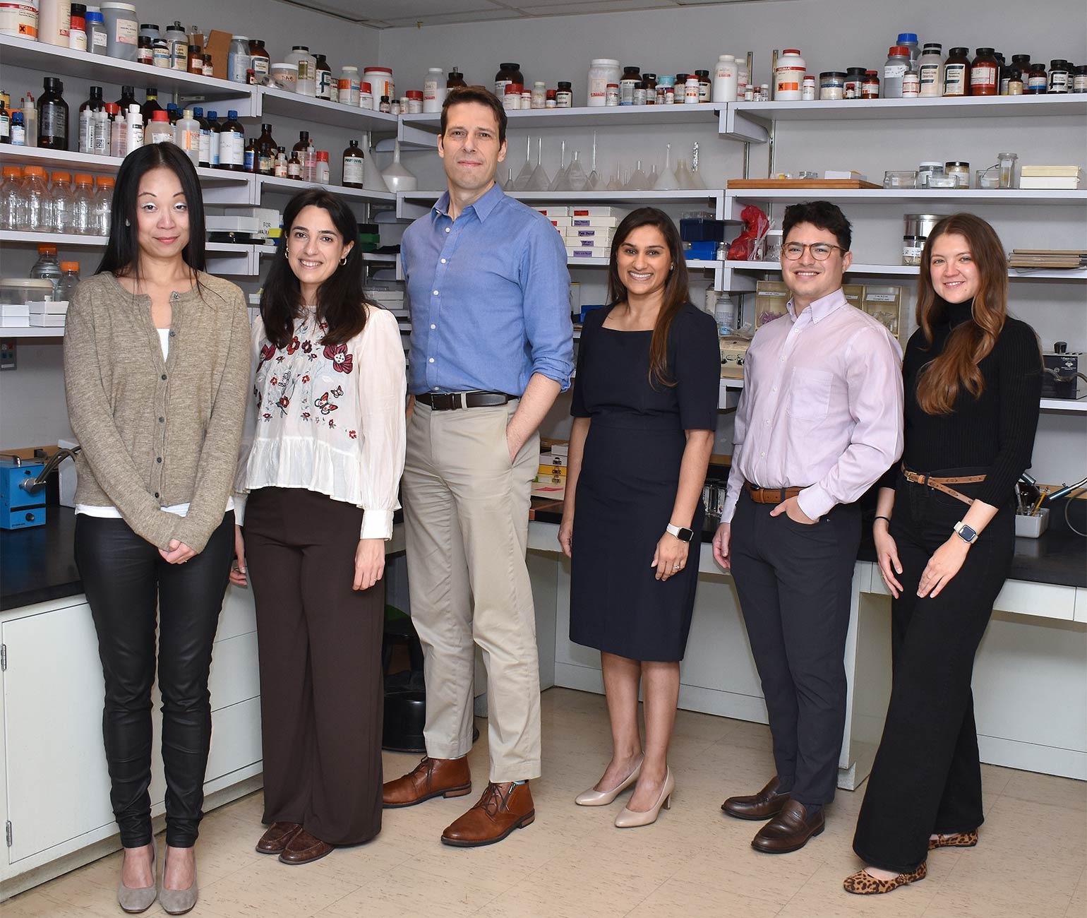 A group of five people in office wear stand in front of a shelf at a lab