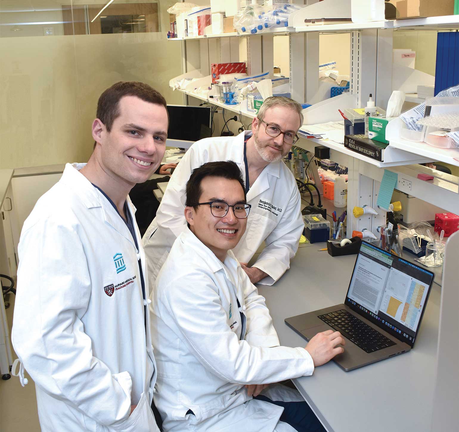 A person in a white lab coat stands in a lab setting