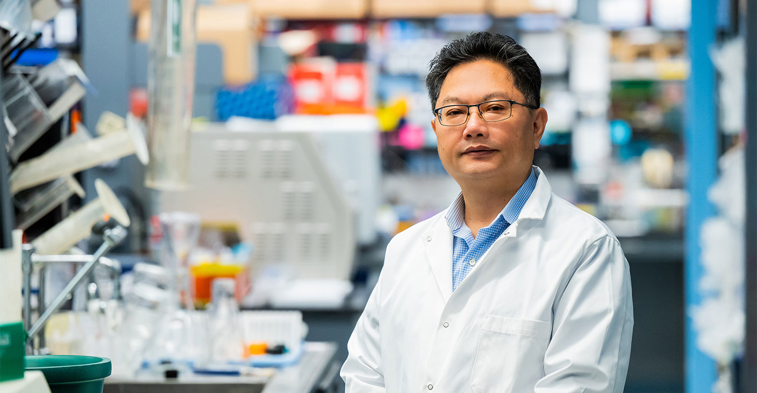 A person in a white lab coat stands in a lab setting